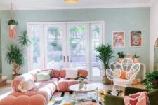 39 a maximalist living room with a green accent wall, a pink sofa, a green chair, a bright rug and a glazed tiered table