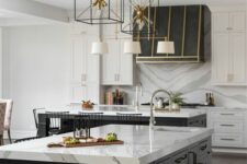 47 a refined white kitchen with shaker cabinets, a large black kitchen island, a hood with gold touches and pendant lamps over the island
