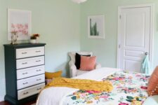 49 a mint-colored bedroom with a bed and floral bedding, a black and white dresser, a neutral chair and a chandelier