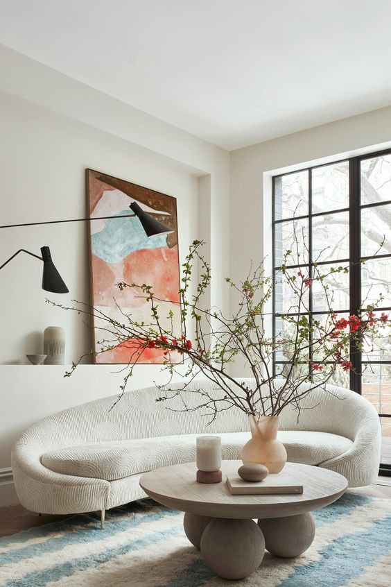 a beautiful neutral living room with a curved sofa, a wooden coffee table, a bold artwork and black lamps