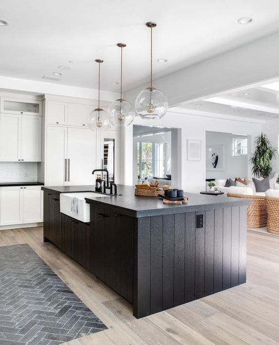 a white kitchen with shaker cabinets, a black slatted kitchen island, glass sphere pendant lamps