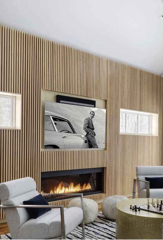 A neutral contemporary living room with a fluted wooden wall, a built in fireplace, a TV and neutral chairs