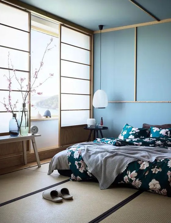 A beautiful blue zen like bedroom with traditional Japanese sliding doors, a low bed and wooden furniture, blue walls and a ceiling, floral bedding