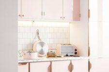a beautiful light pink kitchen with chic brass handles, a white tile backsplash and a terrazzo floor and backsplash