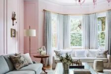 a beautiful pastel living room with pink walls, an aqua green sofa and matching curtains, a glass coffee table and a pretty pink chandelier
