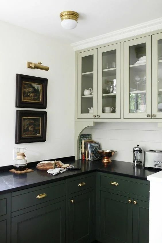 A beautiful two tone green kitchen with a beadboard backsplash, black marble countertops and vintage artwork