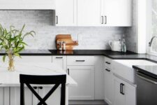 a black and white farmhouse kitchen with shaker cabinets, a marble backsplash and black countertops, black stools
