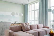 a breezy pastel living room with light green walls, a pink low sofa, a blue coffee table, blue curtains, a marble slab table