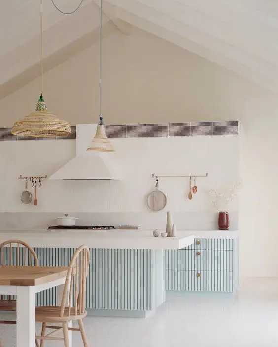 a coastal kitchen with pale blue ridged cabinets and a kitchen island, woven pendant lamps and a white hood that matches the backsplash