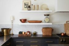 a contrasting navy and white kitchen with a white marble tile backsplash, black countertops and open shelves