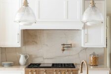 a creamy kitchen with shaker cabinets, a neutral quartz backsplash and countertops, vintage glass pendant lamps