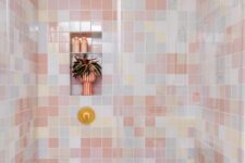 a creative bathroom with mismatching pastel tiles in the shower, white appliances and a gold shower head