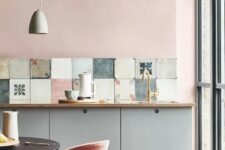 a delicate pastel kitchen with blush walls, grey cabinets, a mismatching tile backsplash and a small eating zone
