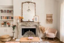 a dreamy living room with a vintage fireplace, a pink sectional and a pink chair, a cane coffee table, a gold chandelier plus books