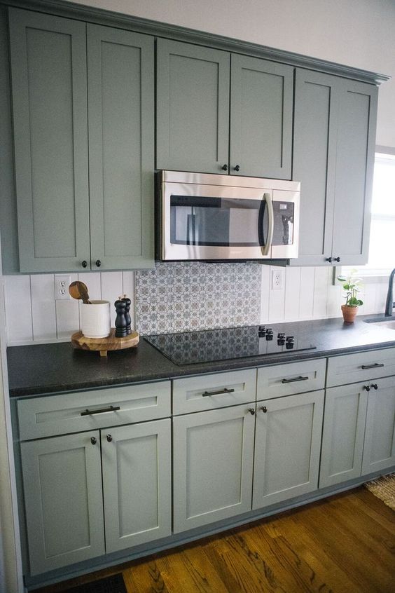 A green shaker style kitchen with a beadboard backsplash and black countertops plus built in appliances