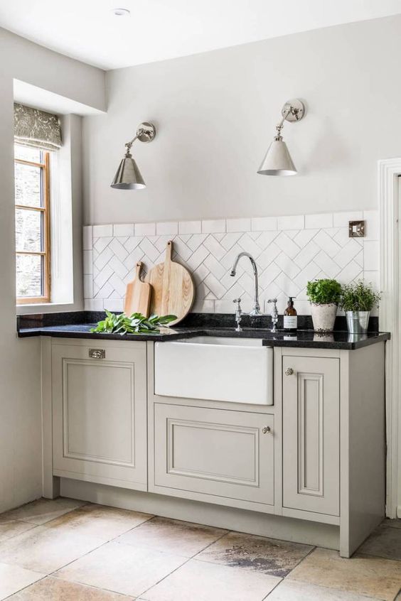 a greige farmhouse kitchen with shaker cabinets, a white tile backsplash, a black countertop and lovely metallic sconces