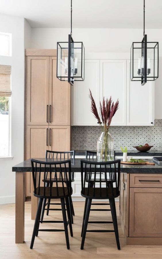 a lovely farmhouse kitchen with stained and white kitchen cabinets, black countertops, pendant black frame lamps