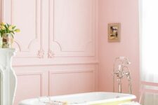 a lovely vintage pastel bathroom with pink walls, a light green fireplace, a pink chair and a yellow clawfoot tub