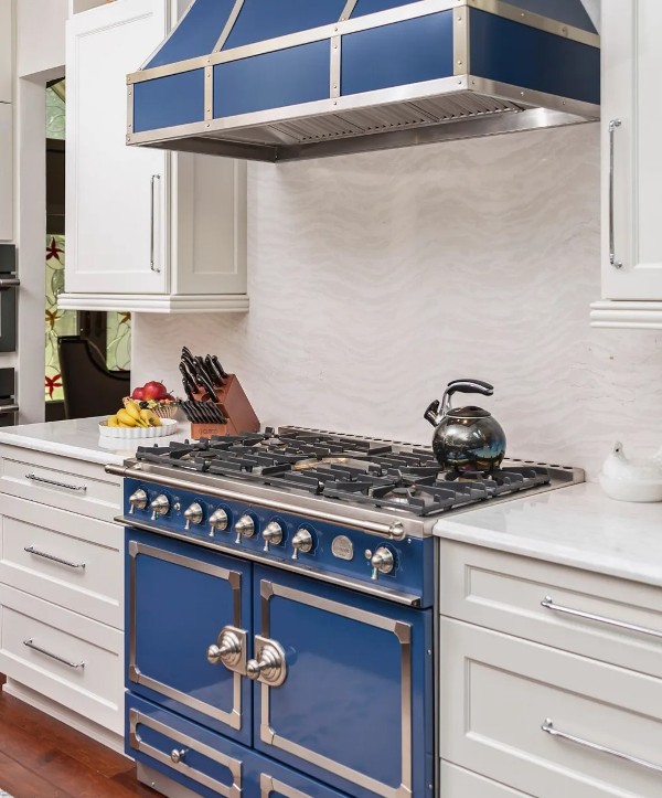 a lovely white kitchen with shaker cabinets, a blue cooker and a hood, a white quartz backsplash and matching countertops