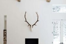 a minimalist fireplace wiht a concrete detail, a firewood storage niche and antlers is a great idea for a minimalist space