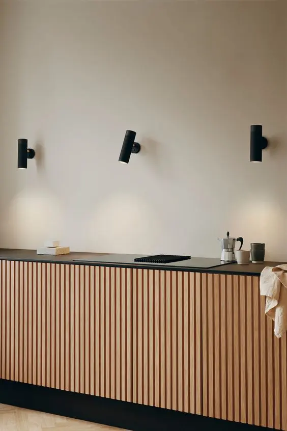 a minimalist kitchen with only a lower row of cabinets with fluted doors, a black countertop and black spotlights over the space