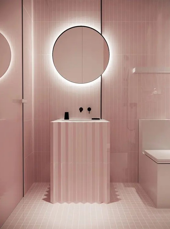 A minimalist light pink bathroom with black touches for depth and a mirror with built in lights