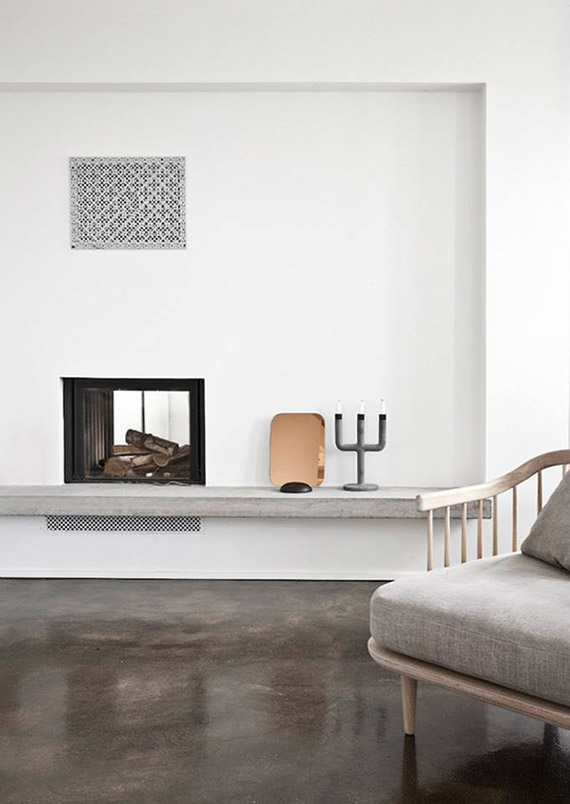 A minimalist neutral space with a built in fireplace, a copper tray and a candelabra, a grey chair is a lovely nook
