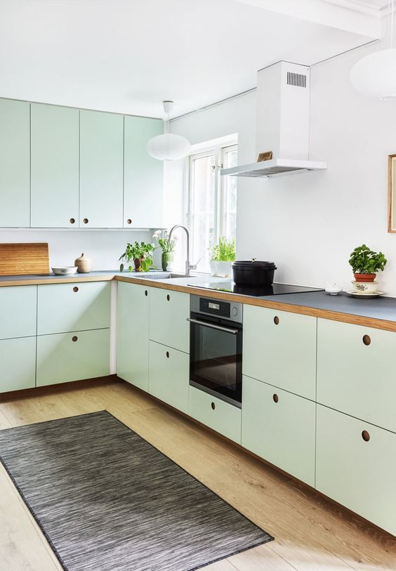 A mint green kitchen with plywood cabinets, a white backsplash, black countertops, no handles and built in appliances