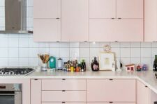 a modern kitchen in light pink, with a white tile backsplash and built-in appliances is all the chic