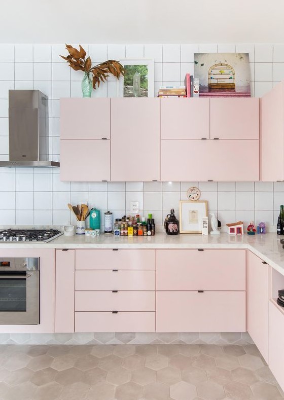 A modern kitchen in light pink, with a white tile backsplash and built in appliances is all the chic