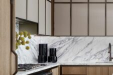 a modern kitchen with beige and stained fluted cabinets, a white marble backsplash and countertops plus black appliances