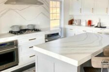 a modern white kitchen with shaker cabinets, a grey kitchen island, a white quratz backsplash and countertops plus a modern chandelier
