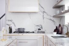 a modern white kitchen with sleek cabinets with gilded edges and a matching hood plus a white quartz backsplash and countertops