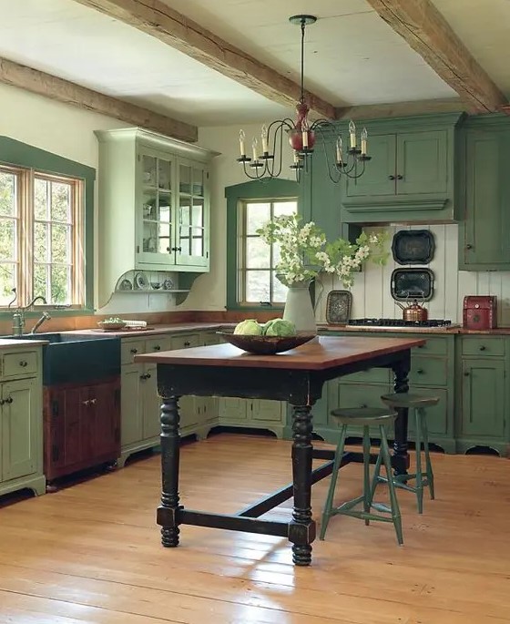 A pastel green vintage inspired kitchen is made cozier with wooden beams and an antique dining table that acts as a kitchen island