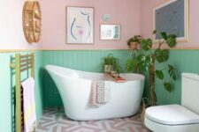 a pretty pastel bathroom with pink and green paneled walls, white appliances, gold touches and lovely artworks is fun
