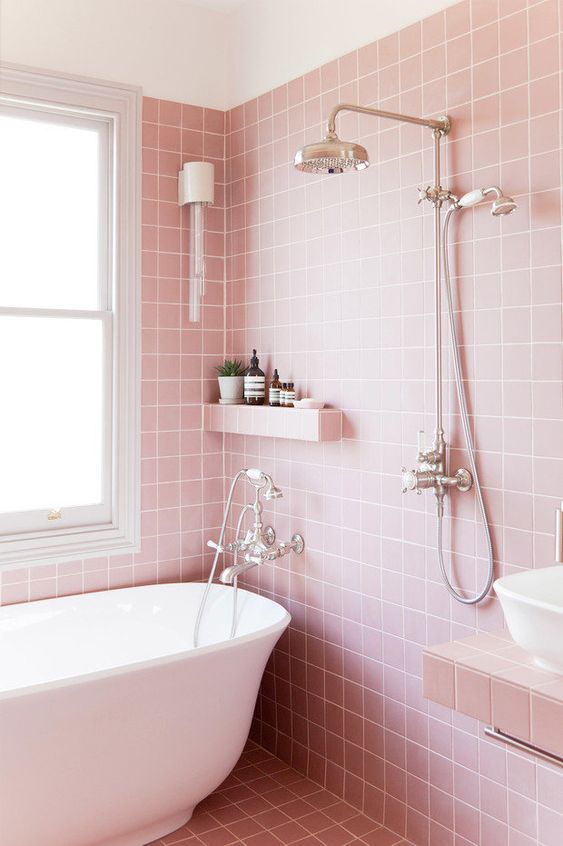 A pretty pink bathroom clad with square tiles, a white tub and a sink, a built in shelf and a vanity plus lights