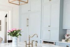a serenity blue kitchen cabinets with white marble countertops and brass touches for a retro look