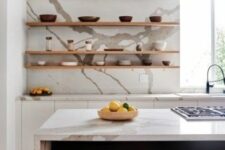 a stylish white kitchen with a navy kitchen island, a white quartz backsplash and countertops and open shelves