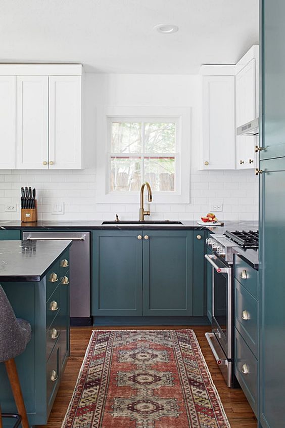 A two tone hunter green and white kitchen with a white subway tile backsplash, black countertops and a bold printed rug