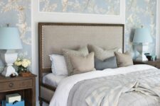 a vintage bedroom with blue printed wallpaper, an upholstered bed with neutral bedding, dark-stained nightstands