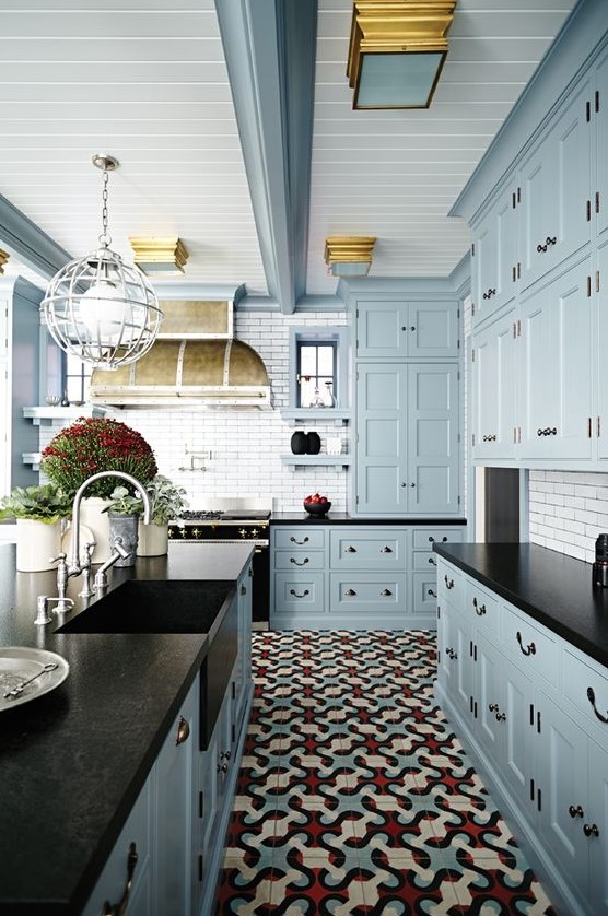 A vintage inspired light blue kitchen with black countertops, a white tile backsplash, potted plants and a vintage hood