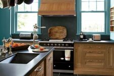 a vintage kitchen with stained cabinets, blue walls, a black backsplash and countertops plus a pan holder over the island