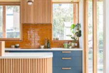 a welcoming warm-colored kitchen with blue cabinets, an orange backsplash and some light-stained cabinets, a curved kitchen island