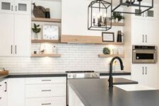 a white farmhouse kitchen with a white tile backsplash, open shelving, black countertops and fixtures for an accent