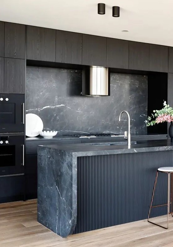 An exquisite kitchen with dark stained cabinets, a black fluted kitchen island, a black marble backsplash and countertops