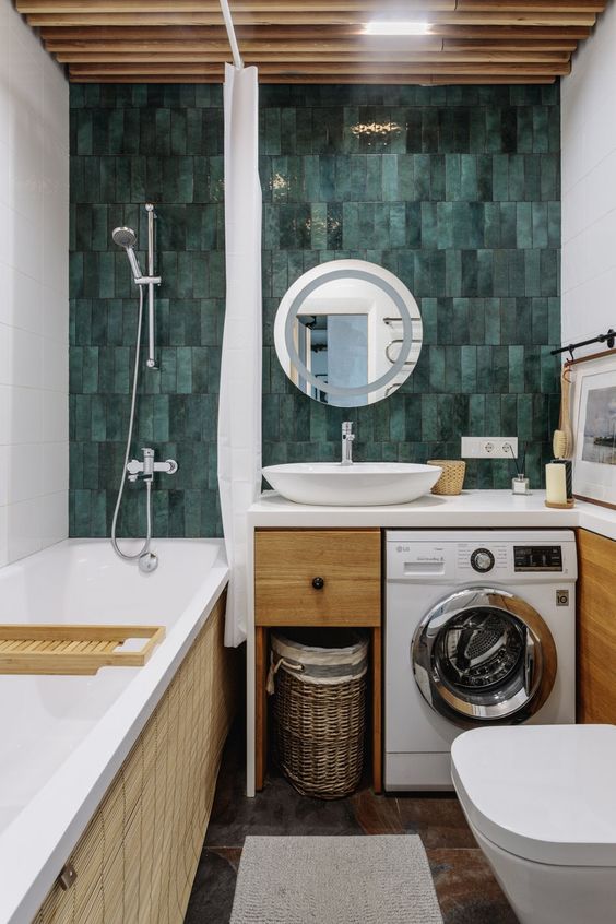 A bright and cool bathroom with a green skinny tile wall, a tub, a timber vanity with a built in washine machine