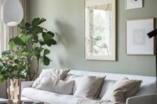 03 a lovely living room with a sage green accent wall, a white sofa and neutral pillows, a gallery wall, a round coffee table and potted plants