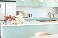 04 a chic mint green slatted kitchen with a white backsplash and countertops, cool pendant lamps, a terrazzo table and stained chairs