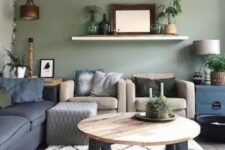 04 a modern boho living room with a sage green accent wall, a navy sofa and tan chairs, a round table and potted plants around