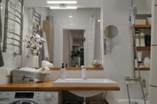 06 a modern white bathroom with a bathtub, an open timber vanity with a washing machine, a mirror and built-in shelves
